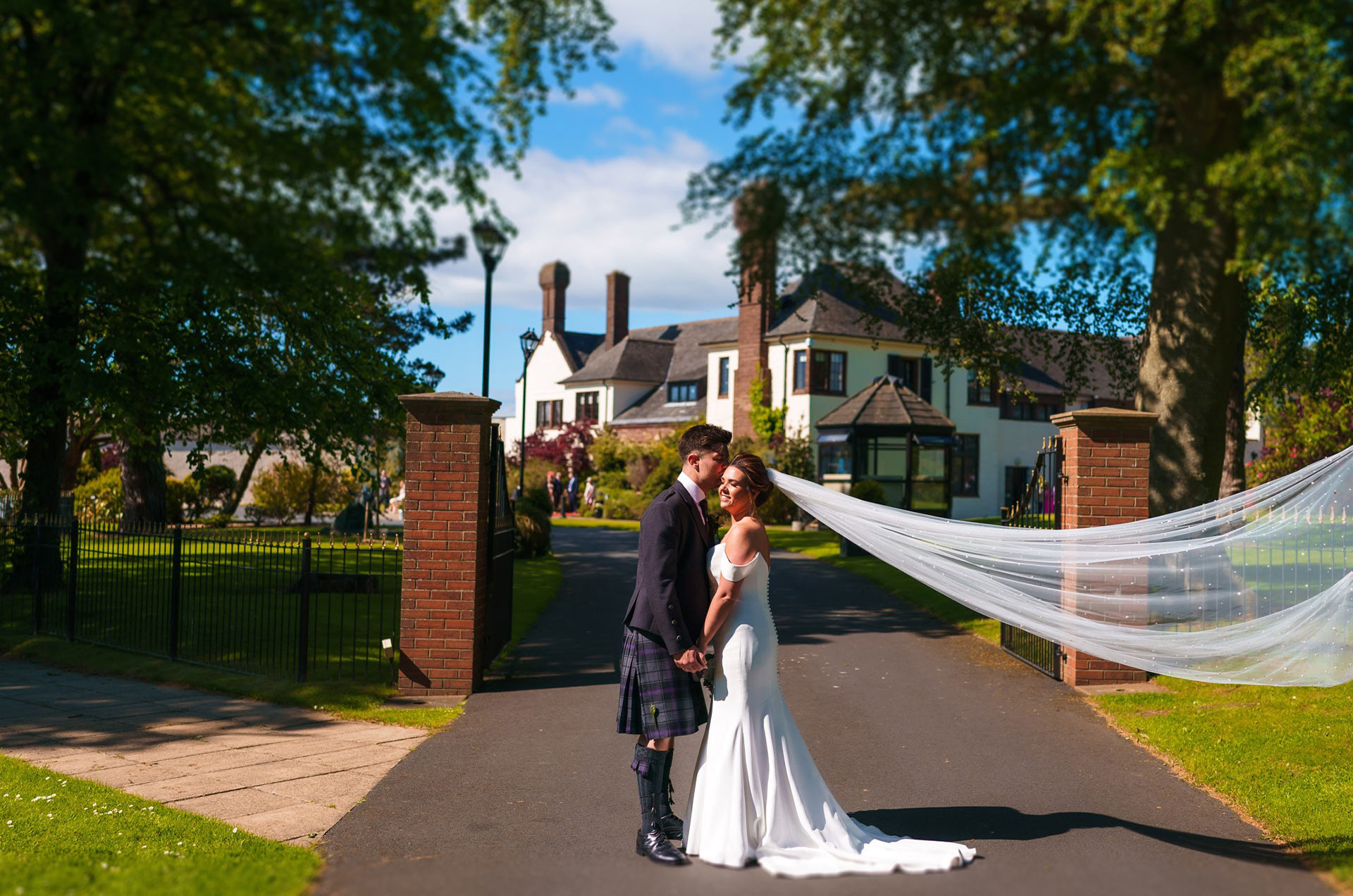 Wedding couple at leading Ayr wedding venue Western House Hotel, photographed in the gardens with the driveway and hotel behind